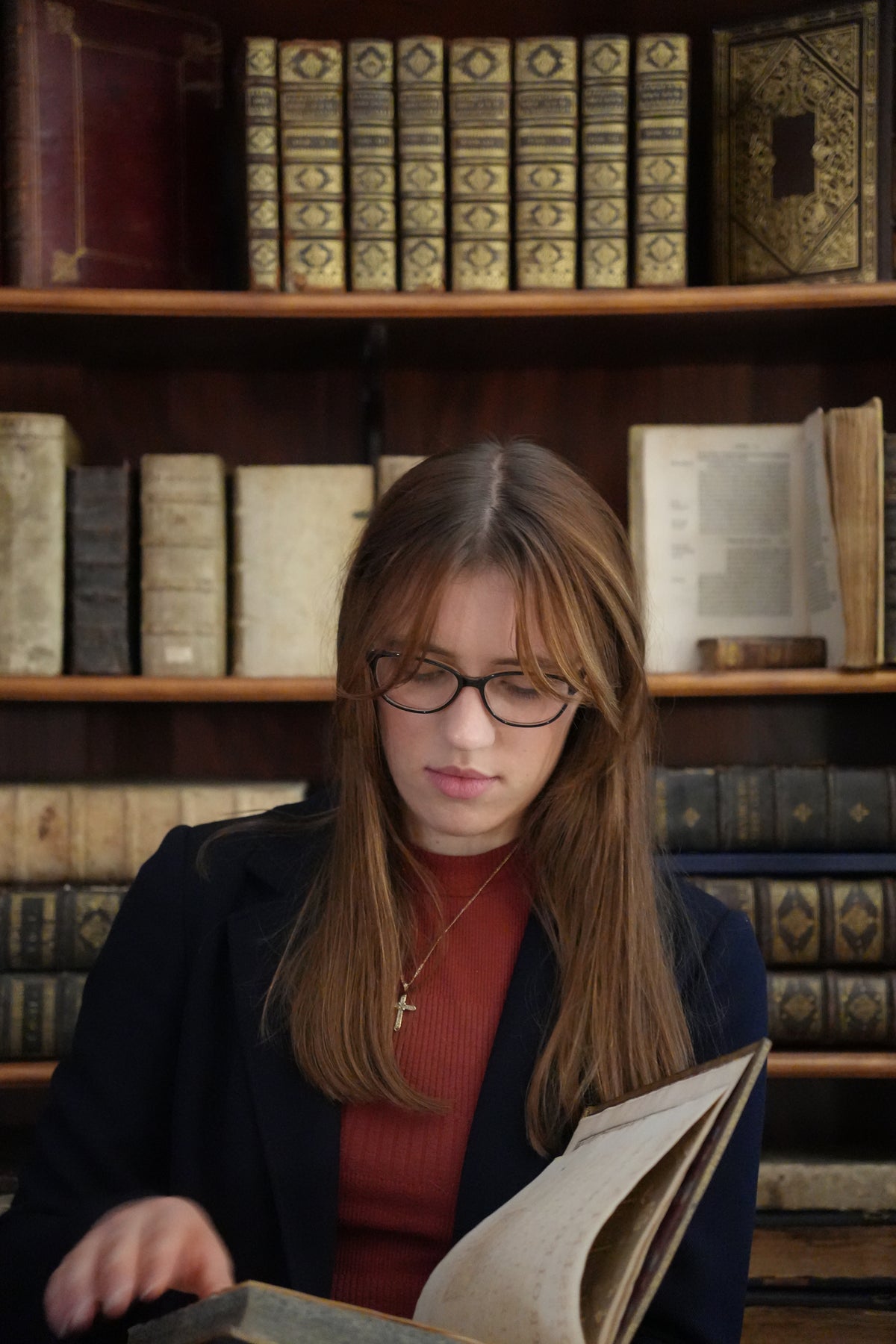 Julia Woodward (of Julia Woodward Antykwariat) reading an antiquarian book in front of a bookcase with rare books and manuscripts.